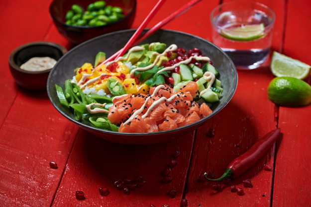 Stor svart skål med poke av laks, mango, avokado, vårløk og agurk